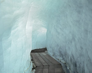 Photographie d'un chemin de bois sous la glace bleue d'un glacier.